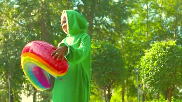 Modern afro woman in green hijab with bright make up and piercing nose hokding rainbow air balloon in summer pak outdoors. — Stock Video
