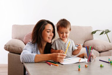 Genç ve güzel bir kadın iki yaşındaki oğluna evde resim yapmayı öğretiyor. Küçük kızıyla kaliteli zaman geçiren bir kadın. Kapat, kopyala boşluk, arkaplan.