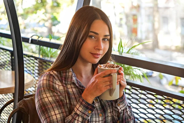 Portrait of young beautiful woman enjoying cup of cocoa w/ marshmallow topping at restaurant. Joyful female experiencing satisfaction from drinking hot beverage on cold autumn day. Close up copy space