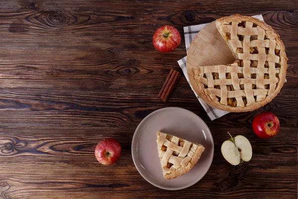 Traditional American Thanks Giving pie with whole organic apples, cinnamon sticks on wooden table. Homemade fruit tart baked to golden crust. Close up, copy space, top view, background.