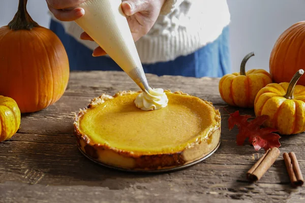 Traditional thanksgiving food on wooden table. Woman adding whipped topping to a delicious homemade pumpkin pie with crust. Top view, close up, copy space, background