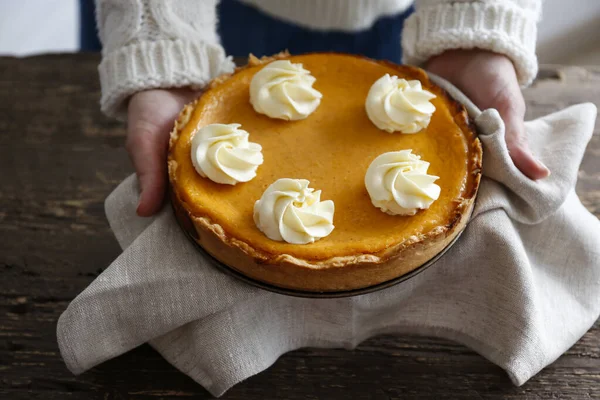 Traditional thanksgiving food concept. Woman in white knitted sweater holding a delicious homemade pumpkin pie with crust. Top view, close up, copy space, background