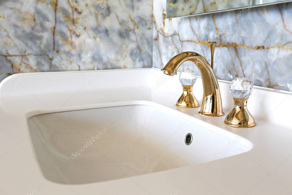 Close up shot of a vintage two handle faucet in a bathroom with marble textured tiles. Copper retro styled water mixer. Copy space, background