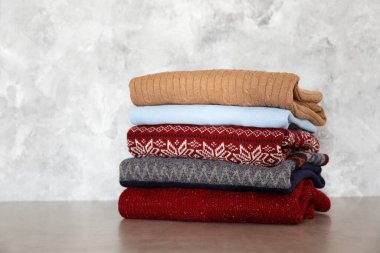 Geleneksel Noel şablonlu bir yığın mükemmel katlanmış süveter. Tahta masada farklı forma ve kazak yığınları, beton duvar arkaplanı. Kapat, üst görünüm, boşluğu kopyala.