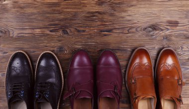 Arka arkaya bir sürü farklı tarz erkek ayakkabısı. Yakın çekim chukka çizmeleri, tek ve çift katlı keşiş kayışlı okfordlar, kahverengi, siyah ve bordo broglar. Üst görünüm, kopyalama alanı, düz görünüm, tahta arkaplan