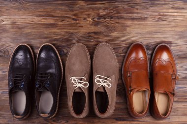 Arka arkaya bir sürü farklı tarz erkek ayakkabısı. Yakın çekim chukka çizmeleri, tek ve çift katlı keşiş kayışlı okfordlar, kahverengi, siyah ve bordo broglar. Üst görünüm, kopyalama alanı, düz görünüm, tahta arkaplan