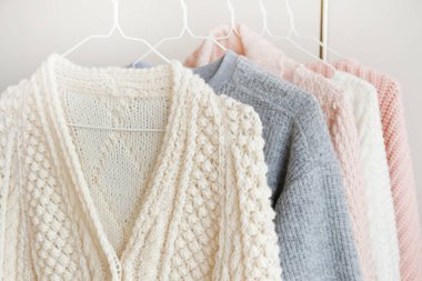 Bir sürü örülmüş sıcak pastel renkli süveter askıda farklı dikey örgü desenleri asılı, açıkça görülebilir doku. Şık sonbahar kış mevsimi örgü giysileri. Kapat, boşluğu kopyala