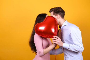 Sevgililer Günü konseptin kutlu olsun. Birbirlerine aşık çiftlerin kalp şeklinde bir balonu tutarken çekilmiş bir fotoğraf. 14 Şubat, sevgililer günü. Sarı duvar arkaplanı, kopyalama alanı, ön görünüm portresi.