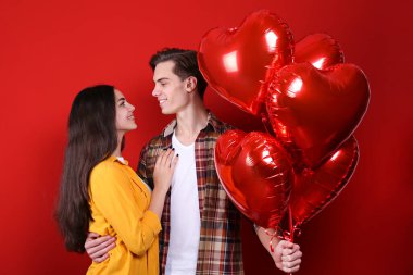 Sevgililer Günü konseptin kutlu olsun. Birbirlerine aşık çiftlerin, ellerinde kalp şeklinde balonlar tutarken çekilmiş bir stüdyo fotoğrafı. 14 Şubat, sevgililer günü. Kırmızı duvar arkaplanı, kopyalama alanı, portre.