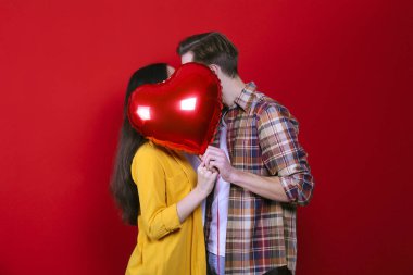 Sevgililer Günü konseptin kutlu olsun. Birbirlerine aşık çiftlerin kalp şeklinde bir balonu tutarken çekilmiş bir fotoğraf. 14 Şubat, sevgililer günü. Kırmızı duvar arkaplanı, kopyalama alanı, ön görünüm portresi.