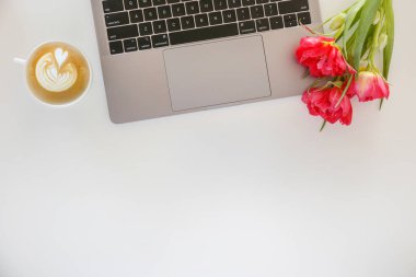 Taze çiçek kompozisyonu, gri dizüstü bilgisayarın yanında soluk pembe arka planı olan bir buket Fransız lalesi. Ofis aşkı konsepti. Boşluğu kopyala, kapat, üst görünüm, düz yatış.