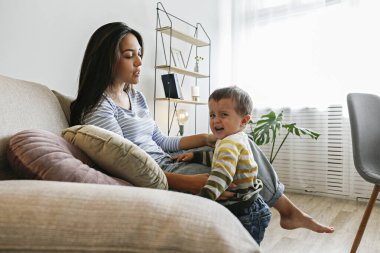 Annesiyle birlikte tekstil kanepesinde ağlayan sevimli bir çocuğun portresi. Üzgün çocuk evde öfke nöbeti geçiriyordu. Yalınayak dikkat çekmek istiyor. Kapat, kopyala boşluk, arkaplan.