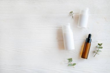 Pompa kapaklı iki farklı boyutta plastik şişe ve bir şişe de damlatıcılı. Etiket yok. Beyaz ahşap masa arka planı. Okaliptüs yapraklarını dekor olarak kullanır. Kapat, üst görünüm, metin veya logo için boşluk kopyala.