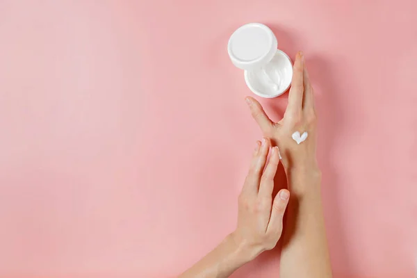 Revitalizing hand cream for healing and recovery after excessive use of soap and disinfectants. Young woman applying moisturizing lotion. Copy space, close up, pink background, flat lay, top view.