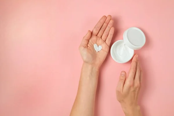 Revitalizing hand cream for healing and recovery after excessive use of soap and disinfectants. Young woman applying moisturizing lotion. Copy space, close up, pink background, flat lay, top view.