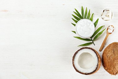 Hindistan cevizi bir gıda kaynağı ve kozmetik üründür. Çatlak meyve, bir kavanoz nemlendirici krem, ahşap kaşık ve ahşap desenli masa üzerinde bir palmiye yaprağı. Kapat, üst görünüm, kopyala boşluk, düz alan, arkaplan.