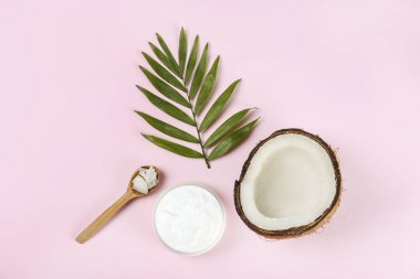 Hindistan cevizi bir gıda kaynağı ve kozmetik üründür. Çatlak meyve, bir kavanoz nemlendirici krema ve pembe masa üstünde bir palmiye yaprağı. Kapat, üst görünüm, kopyala boşluk, düz alan, arkaplan.