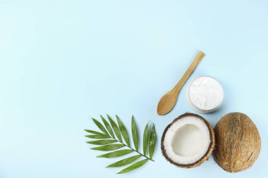 Hindistan cevizi bir gıda kaynağı ve kozmetik üründür. Çatlak meyve, bir kavanoz nemlendirici krem, ahşap kaşık ve mavi masa üstünde bir palmiye yaprağı. Kapat, üst görünüm, kopyala boşluk, düz alan, arkaplan.