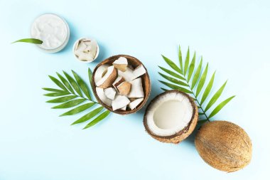 Hindistan cevizi bir gıda kaynağı ve kozmetik üründür. Yarım meyve, bir kavanoz nemlendirici krem ve mavi masa üstünde bir palmiye yaprağı. Kapat, üst görünüm, kopyala boşluk, düz alan, arkaplan.