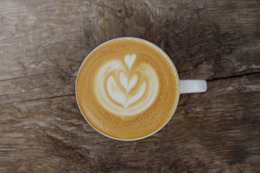 Beyaz bardakla kapuçino, köpüklü sıcak içecek ve ahşap desenli masa tabağı. Latte sanat konsepti. Kapat, metin için boşluk kopyala, tahta arkaplan.