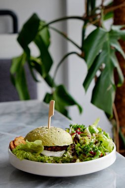 Yeşil ekmekli sebze burger, nohut köftesi, taze sebze, vegan mayonez ve yanında salata. Gaddarca bedava fast food restoranı masası. Tabak dolusu yemek. Kapat, kopyala boşluk, arkaplan.