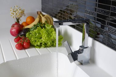 Bir sürü çiğ organik meyve, sebze ve sebzeler lavabonun yanındaki beyaz mutfak tezgahında yığılmıştı. Kapat, metin, arkaplan ve üst görünüm için boşluk kopyala.