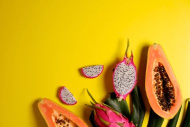 Canavar palmiye yapraklı egzotik meyve kompozisyonu. Papaya ve pitaya, düşük kalorili besleyici meyveler, bütün ve yarı yarıya, görünür posa dokusu, izole edilmiş sarı arkaplan. Kapat, boşluğu kopyala, üst görünüm.
