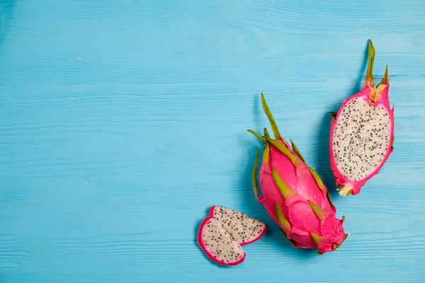 Pitaya - an exotic low-calorie nutrient-dense fruit with high amount of fiber and magnesium. Whole and halved dragon fruit, visible pulp texture on blue wood background. Close up, copy space, top view