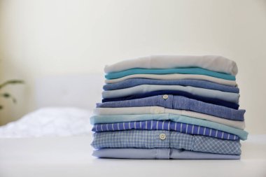 Renkli, mükemmel katlanmış giysi yığını evdeki yatağın üzerinde. Farklı renkte tişörtler ve soluk pembe arka planda izole edilmiş tişörtler. Kapat, boşluğu kopyala.