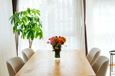 Cam vazoda güzel ranunculuslar olan ahşap yemek masasını yakın plan çek. Bir buket karışık İran düğün çiçeği. Pencereden gelen yumuşak doğal ışık altında. Boşluğu kopyala, kapat, arkaplan.