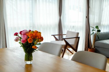 Ahşap masadaki vazoda bir buket karışık ranunculus çiçeği. İskandinav tarzı bir dairede boş bir oturma odası. Uzun pencereleri ve parke döşemeleri var. Kapat, kopyala boşluk, arkaplan.