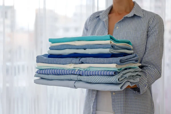 完全に折り畳まれたシャツのスタックを保持自宅で若い女性の作物のショット 彼女の手の中にさまざまな服の山と認識できない女性 洗濯日の概念 スペースをコピーし — ストック写真