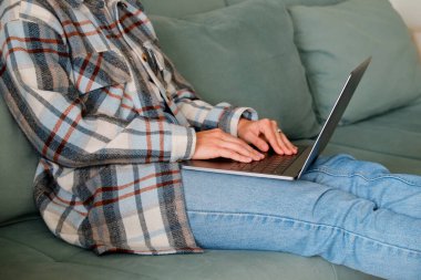 Genç bir kadının dizüstü bilgisayarla uzaktan çalışıp oturma odasındaki mavi kanepede oturduğu yakın çekim. Klavyede elleri olan serbest çalışan bir kadın. Boşluğu kopyala, arkaplan