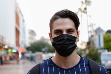 Tek kullanımlık maske takan Arap kökenli yakışıklı bir adamın portresi sokaklardaki bulaşıcı maddelerle temastan korunmak için bariyer görevi görüyor. Kapat, kopyala boşluk, arkaplan.