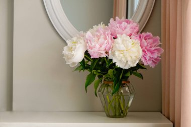 Gri duvar arkaplanının üzerinde cam bir vazoda duran güzel şakayık çiçeklerinin bir stüdyo fotoğrafı ve metin için bir sürü fotokopi alanı. Kadınsı çiçek kompozisyonu. Kapat, arkaplan.