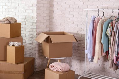 Boş, imzasız, taşınmamış kutular ve yeni boş bir dairede askıda asılı giysiler. Geniş mobilyalı, paketsiz karton kutu yığını olan bir oda. İç arkaplan, metin için kopyalama alanı.