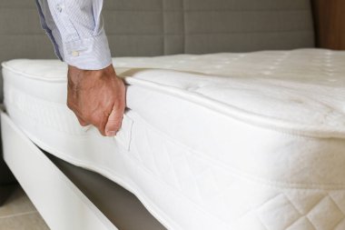 Yeni yatak teslimatı ve montaj hizmeti konsepti. Ortopedik köpük yatağı müşterinin yatak odasındaki leşin üzerine sererken erkek işçinin ellerinin kırpılmış görüntüsü. Kapat, kopyala boşluk, arkaplan.