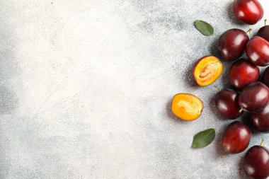 Sulu organik bir bütünün ve yeşil yapraklı yarım eriklerin görüntüsünü kapat. Görünür çekirdek dokusu, homurdanmış taş arka planı, kopyalama alanı. Meyve dilimlerinden makro shot. Üst manzara, düz uzanma.