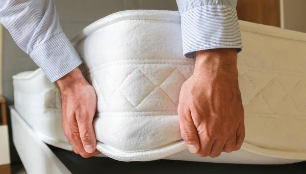 New bed delivery and assembly service concept. Cropped shot of male worker\'s hands in process of laying the orthopedic foam mattress on carcass in customer\'s bedroom. Close up, copy space, background.