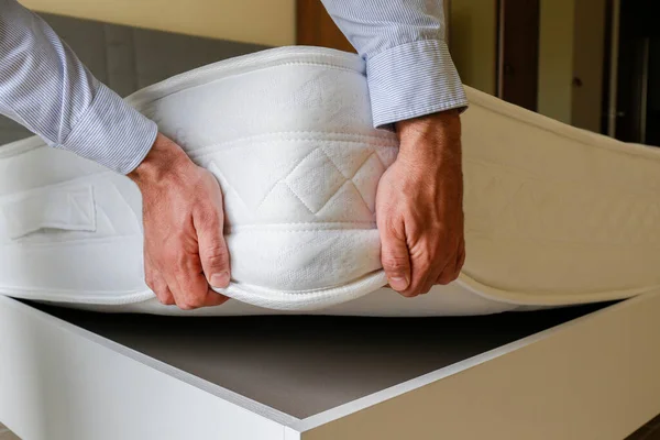 New bed delivery and assembly service concept. Cropped shot of male worker\'s hands in process of laying the orthopedic foam mattress on carcass in customer\'s bedroom. Close up, copy space, background.