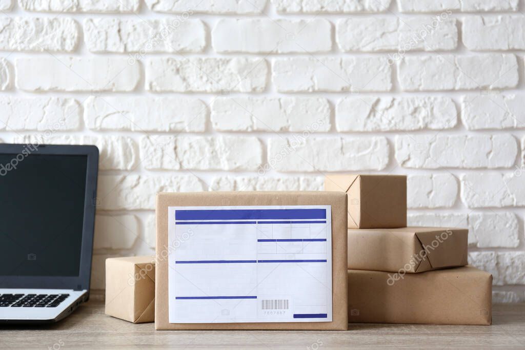 Stacked packages of different sizes wrapped in craft paper with shipping labels. Laptop and parcels on table. Shipping software for ecommerce fulfillment concept. Close up, copy space, background.