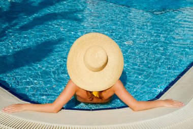 Sarı bikini mayo ve geniş kenarlı hasır şapka takan, yüzme havuzunda serinleyen, sağlıklı vücutlu, tanımlanamayan beyaz kadın. Boşluğu kopyala, üst görünüm.