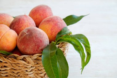 Hasır bir kasede bir sürü olgun organik şeftali, beyaz ahşap masa arkaplanı. Yerel halk sepetin içinde meyve üretiyor. Temiz yeme konsepti. Üst görünüm, kapat, metin için alanı kopyala.