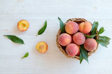Hasır bir kasede bir sürü olgun organik şeftali, beyaz ahşap masa arkaplanı. Yerel halk sepetin içinde meyve üretiyor. Temiz yeme konsepti. Üst görünüm, kapat, metin için alanı kopyala.
