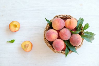 Hasır bir kasede bir sürü olgun organik şeftali, beyaz ahşap masa arkaplanı. Yerel halk sepetin içinde meyve üretiyor. Temiz yeme konsepti. Üst görünüm, kapat, metin için alanı kopyala.