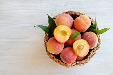 Hasır bir kasede bir sürü olgun organik şeftali, beyaz ahşap masa arkaplanı. Yerel halk sepetin içinde meyve üretiyor. Temiz yeme konsepti. Üst görünüm, kapat, metin için alanı kopyala.