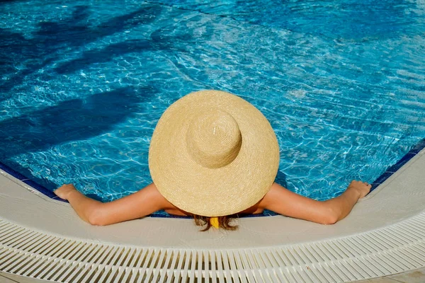 Unrecognizable caucasian woman with fit body wearing yellow bikini bathing suit and broad brim straw hat covering her face, chilling in a swimming pool. Copy space, top view.