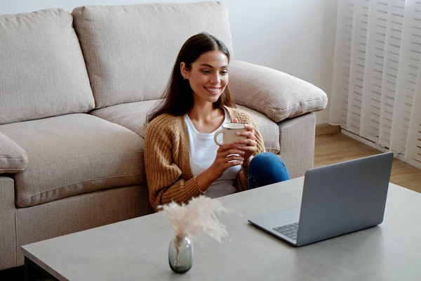 Young beautiful woman sitting alone at home and enjoying alone time with her laptop. Portrait of female sitting on the floor and watching shows on a streaming service. Close up, copy space, background