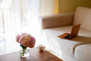 Merkez ofis konsepti. Memleketten atanmış bir iş. Kahve fincanı olan kadınsı çalışma alanı, masada çiçekler ve koltukta modern dizüstü bilgisayar. Kapat, kopyala boşluk, arkaplan.