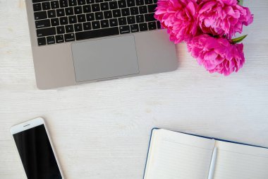 Laptop bilgisayar klavyesi, boş ekran cep telefonu, doldurulmamış planlama defteri ve ahşap desenli masa üzerindeki yazı için bir sürü kopya alanı olan şakayık çiçekleri. Yakın çekim, üst görüş, kırpılmış çekim